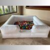 Alberca inflable blanca llena de pelotas multicolor colocada en interior con piso de mármol