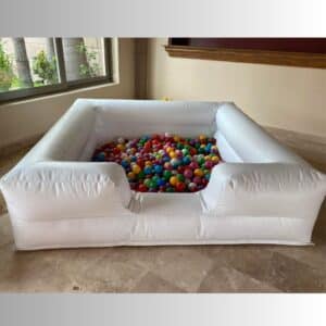 Alberca inflable blanca llena de pelotas multicolor colocada en interior con piso de mármol