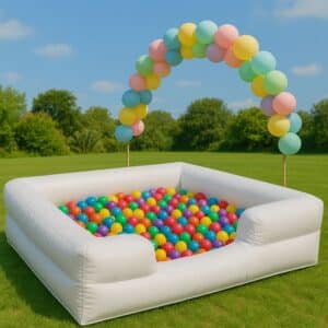 Alberca inflable blanca con pelotas multicolor y decoración de globos en forma de arco, colocada en jardín