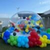 Burbuja inflable para jardín decorada con globos de colores llamativos debajo de una pérgola de madera.