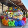 Burbuja inflable para jardín decorada con globos de colores llamativos, colocada dentro de una sección al aire libre de una casa.