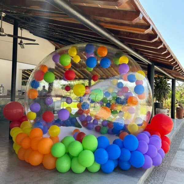 Burbuja inflable para jardín decorada con globos de colores llamativos, colocada dentro de una sección al aire libre de una casa.