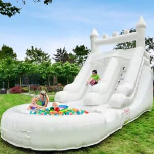 Niños jugando en castillo inflable blanco con doble resbaladilla y alberca frontal llena de pelotas