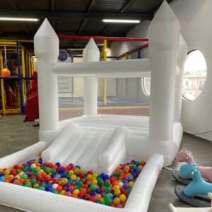 Castillo inflable blanco decorado con globos, ideal para fiestas infantiles y eventos especiales